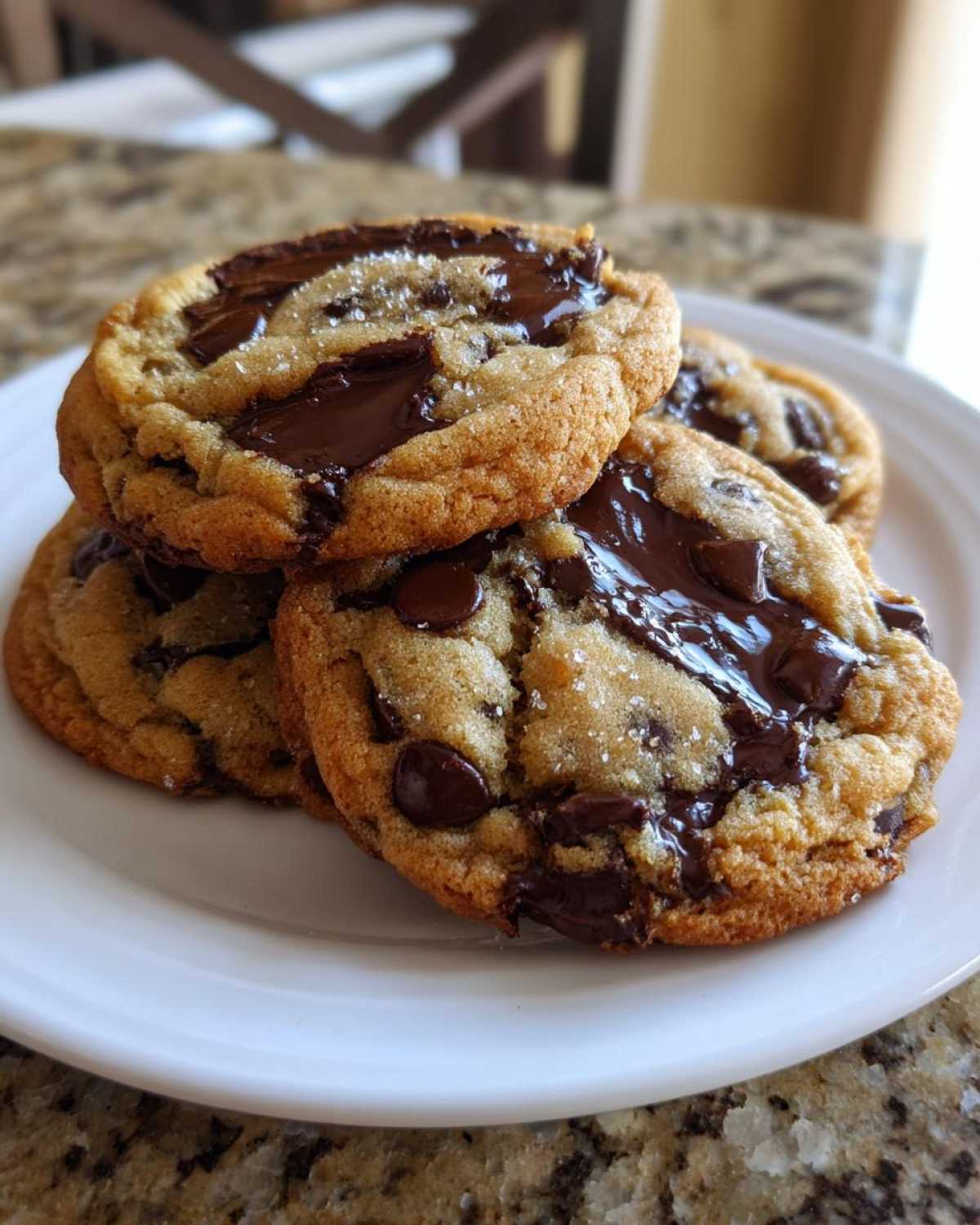 A stack of three perfectly chewy chocolate chip cookies with melted chocolate pools and sea salt.