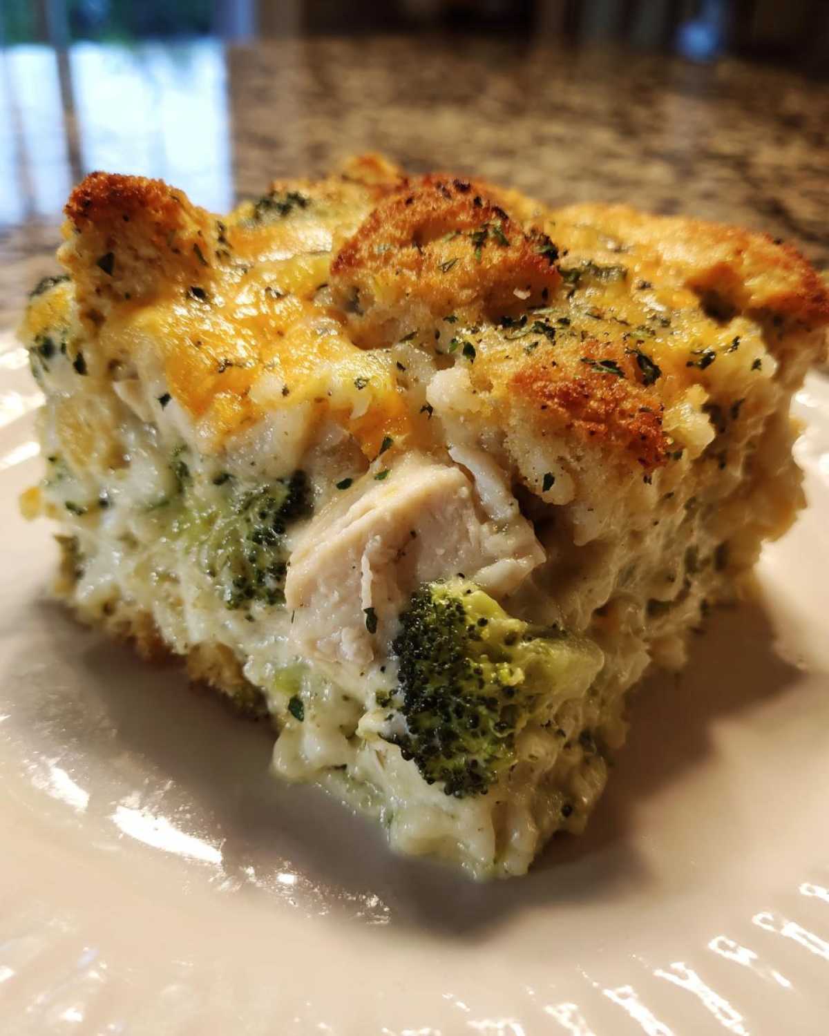 A close-up of a square serving of creamy chicken broccoli rice casserole with a golden, crunchy topping.