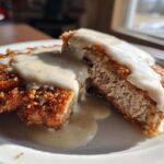 A close-up of a cross-section of crispy chicken fried steak smothered in white country gravy.