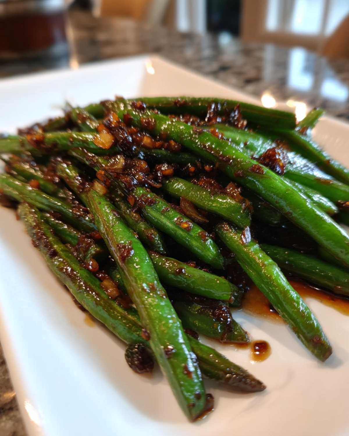 Close-up of vibrant green beans coated in a dark, savory garlic sauce, ready to serve.
