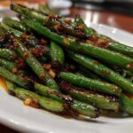 A close-up of vibrant green beans coated in a savory, dark garlic sauce, ready to serve.