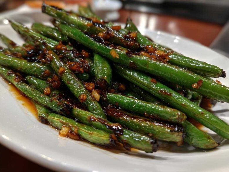 A close-up of vibrant green beans coated in a savory, dark garlic sauce, ready to serve.