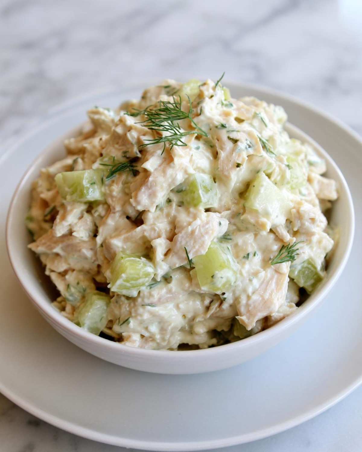 A close-up of creamy cottage cheese chicken salad mixed with chunks of cucumber, garnished with fresh dill.