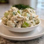 A serving of creamy cottage cheese chicken salad with visible celery chunks, topped with fresh dill.