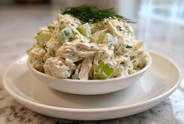 A serving of creamy cottage cheese chicken salad with visible celery chunks, topped with fresh dill.