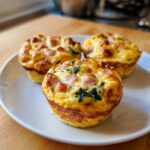 Three golden baked cottage cheese egg cups with ham and spinach on a white plate.