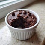 A bite taken out of a rich, dark Cottage Cheese Microwave Brownie topped with chocolate chips in a white ramekin.