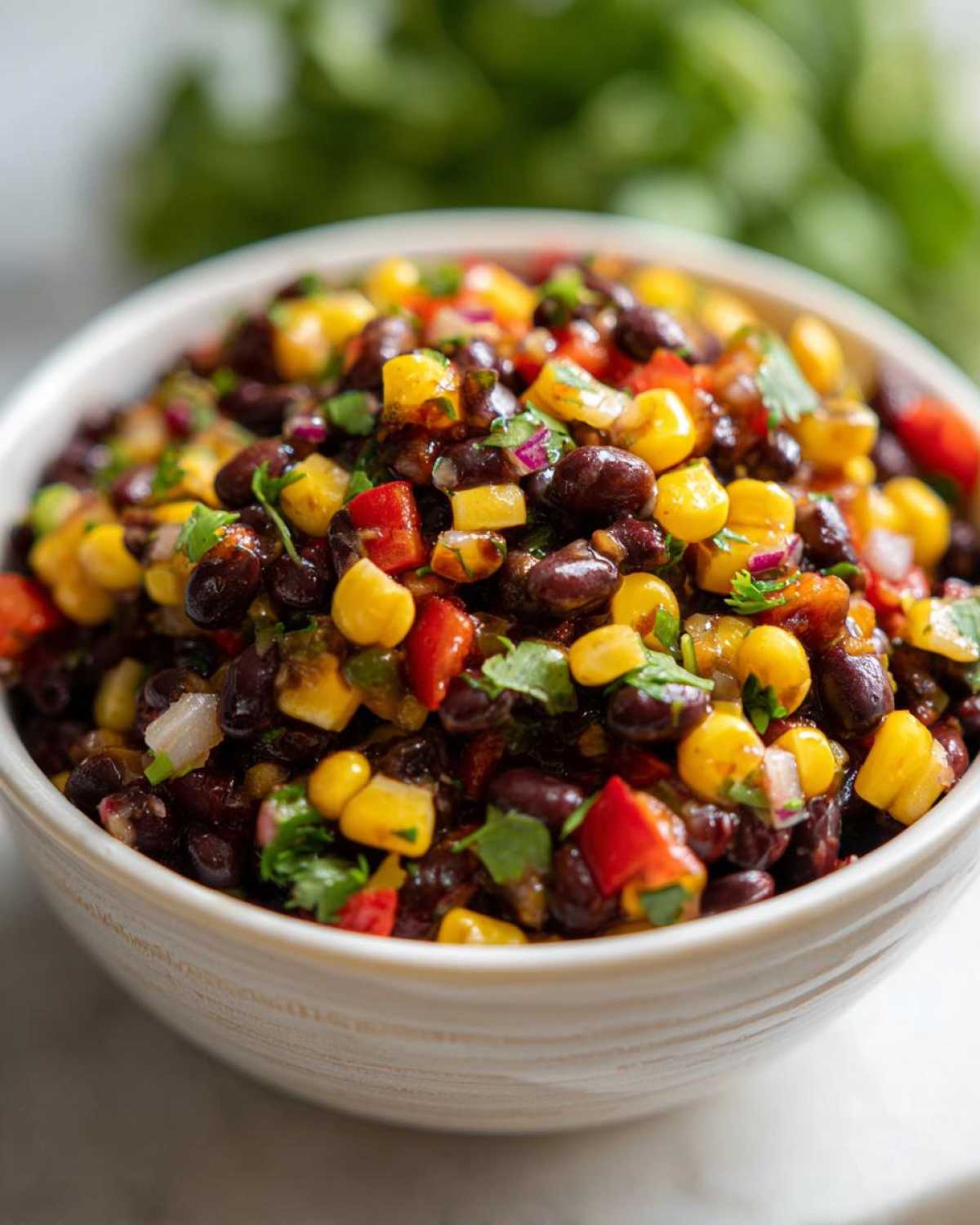 Close-up of a white bowl filled with vibrant cowboy caviar featuring black beans, corn, red peppers, and cilantro.