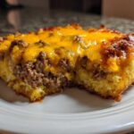 A close-up of a hearty slice of cowboy cornbread casserole featuring a layer of seasoned ground beef topped with melted cheddar cheese.