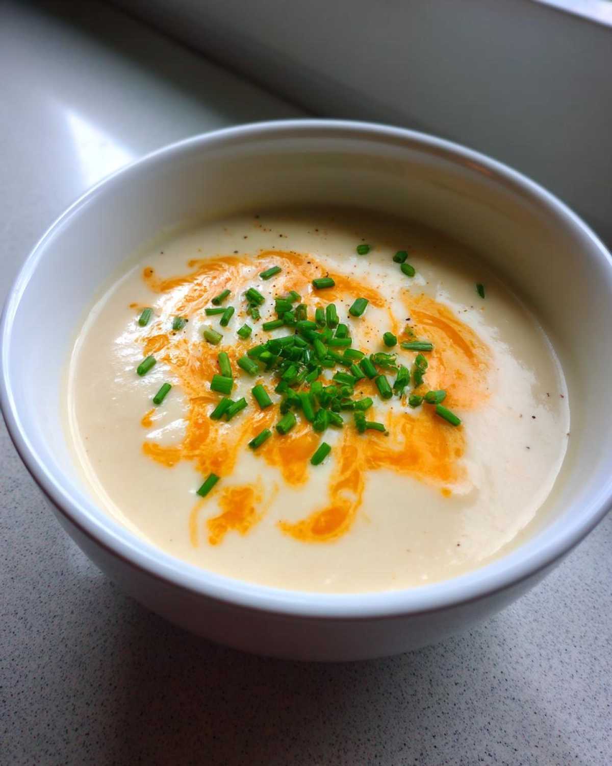 A close-up of creamy cauliflower soup topped with swirls of orange oil and fresh chopped chives.