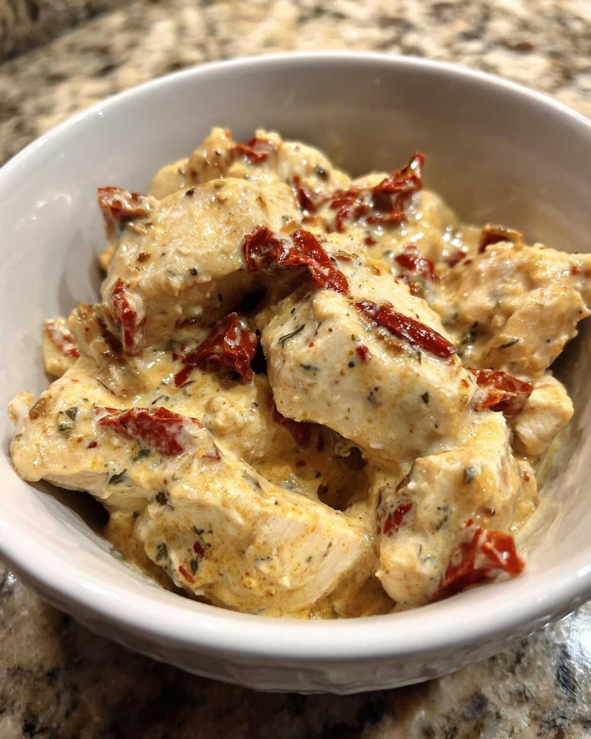Close-up of tender chicken pieces smothered in creamy sauce with sun-dried tomatoes, part of the crockpot marry me chicken recipe.