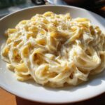 Close-up of fettuccine pasta coated in rich, creamy Olive Garden Alfredo sauce and sprinkled with black pepper.