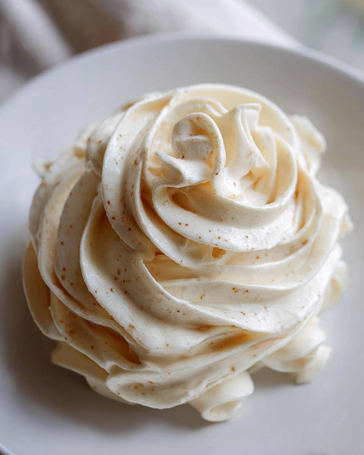 Close-up of a thick swirl of creamy homemade alfredo sauce, showing flecks of black pepper, on a white plate.