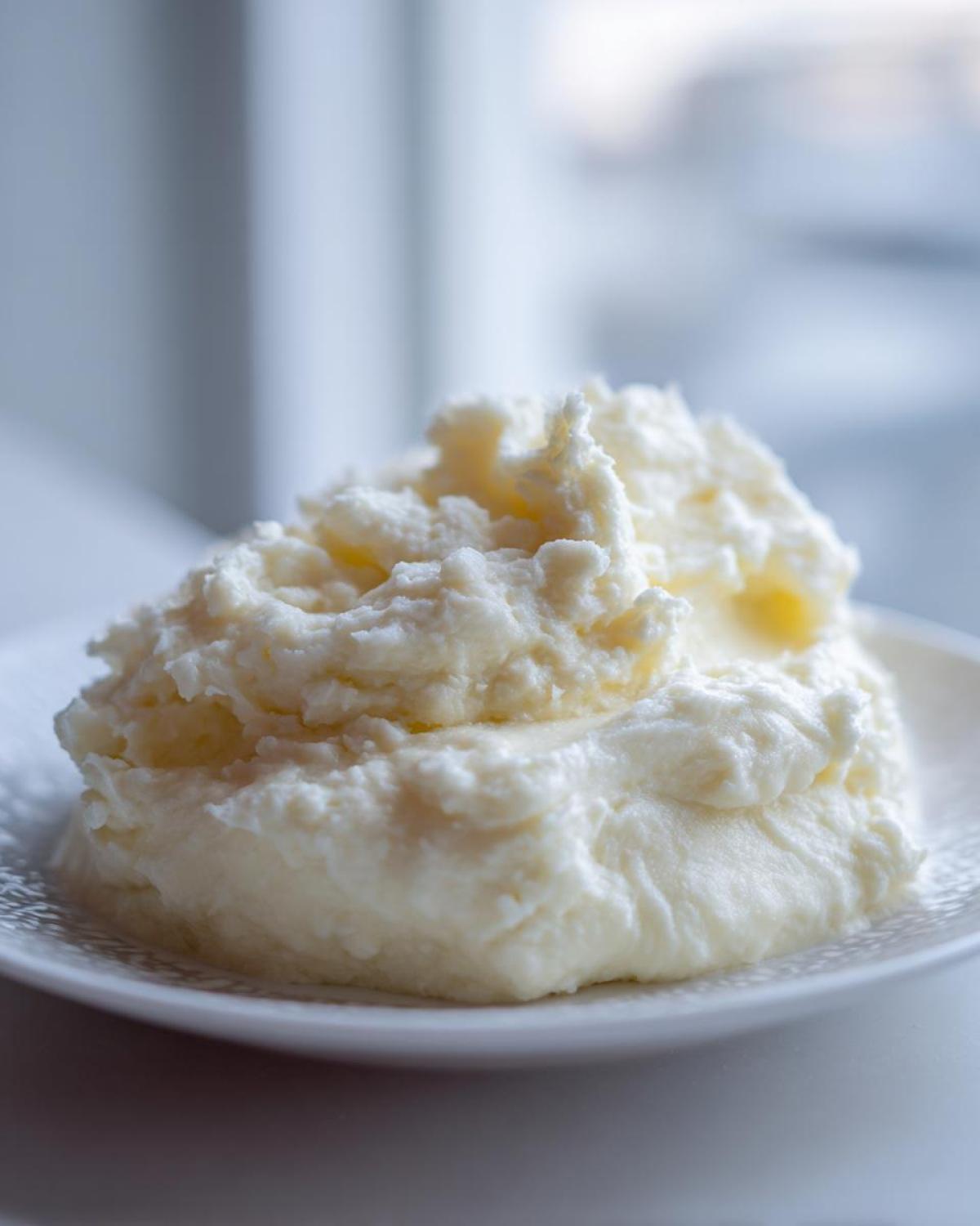 Close-up of a dollop of thick, creamy white mixture, resembling homemade alfredo sauce or rich mashed potatoes.