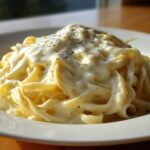 A close-up of fettuccine pasta generously coated in rich, creamy Olive Garden Alfredo sauce and sprinkled with pepper.