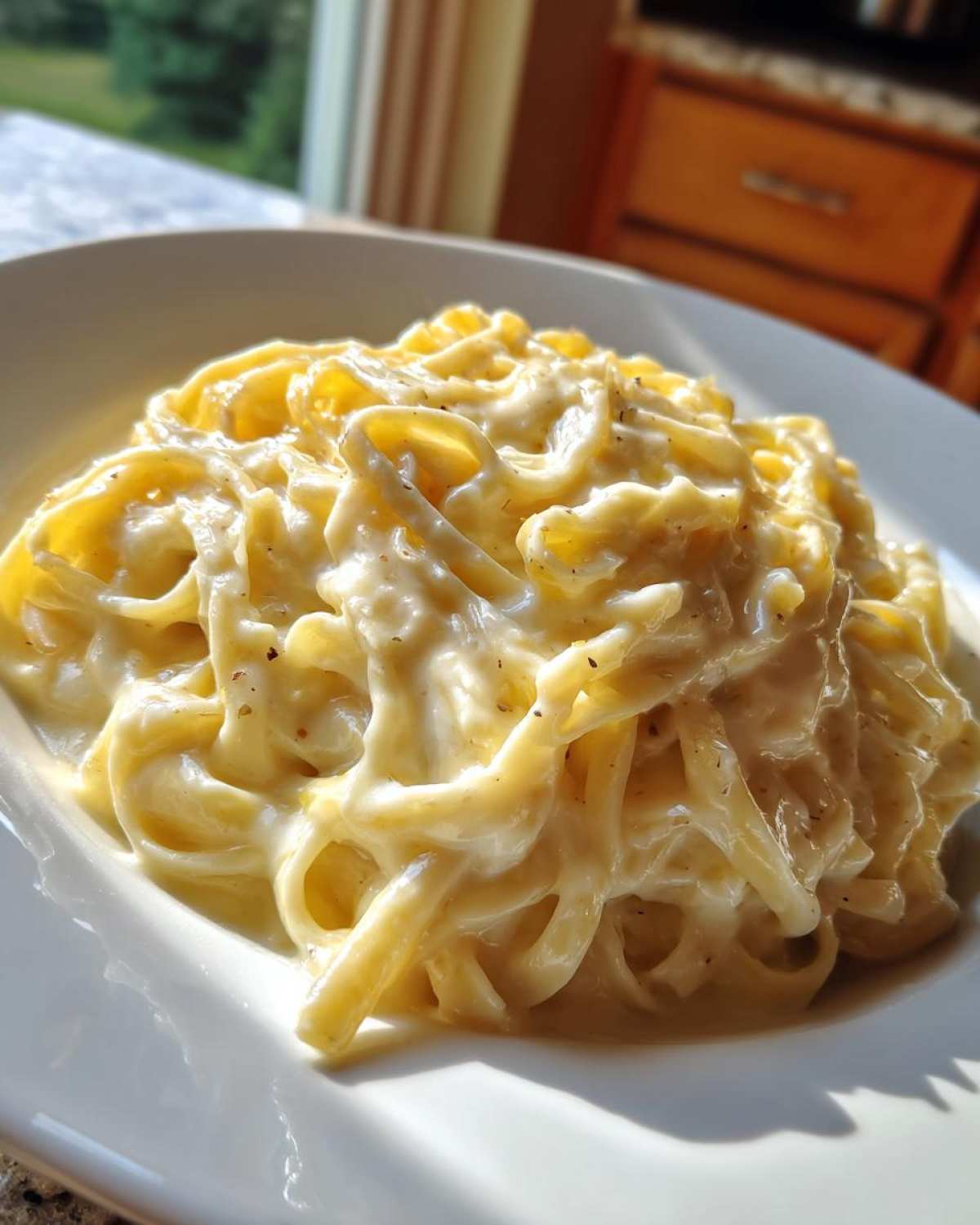 Close-up of fettuccine pasta generously coated in creamy Olive Garden Alfredo Sauce, served on a white plate.