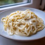 Close-up of spaghetti generously coated in creamy homemade alfredo sauce and topped with grated Parmesan cheese.
