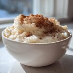 A close-up of creamy rice pudding served in a white bowl, generously topped with ground cinnamon.