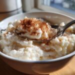 Close-up of creamy rice pudding recipe topped with ground cinnamon in a white bowl with a spoon.