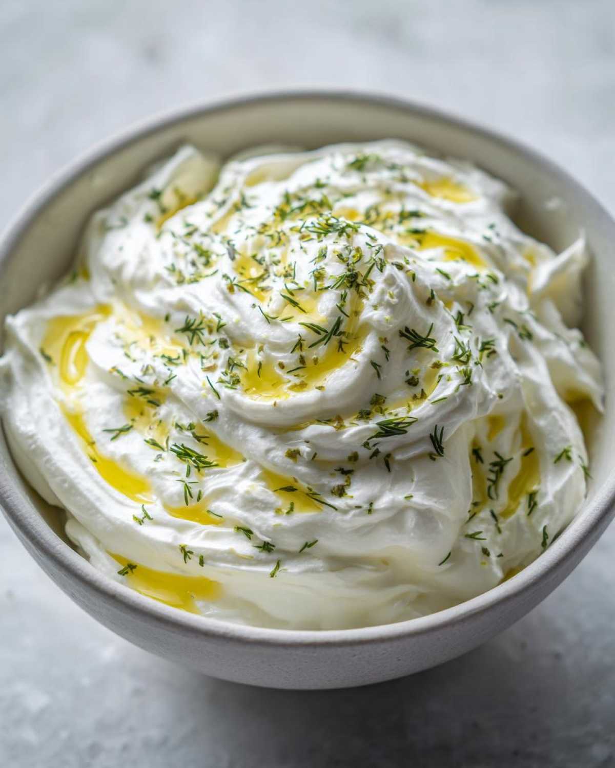 Close-up of creamy whipped feta dip topped with olive oil and fresh dill.