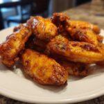 A close-up of several glossy, golden-brown crispy air fryer chicken wings piled on a white plate.