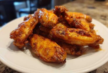 A close-up of several glossy, golden-brown crispy air fryer chicken wings piled on a white plate.