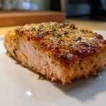 Close-up of a perfectly cooked piece of air fryer salmon with a golden, crispy, herb-crusted top.