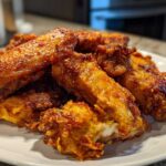A close-up of a pile of perfectly crispy, golden-brown chicken wings served on a white plate.
