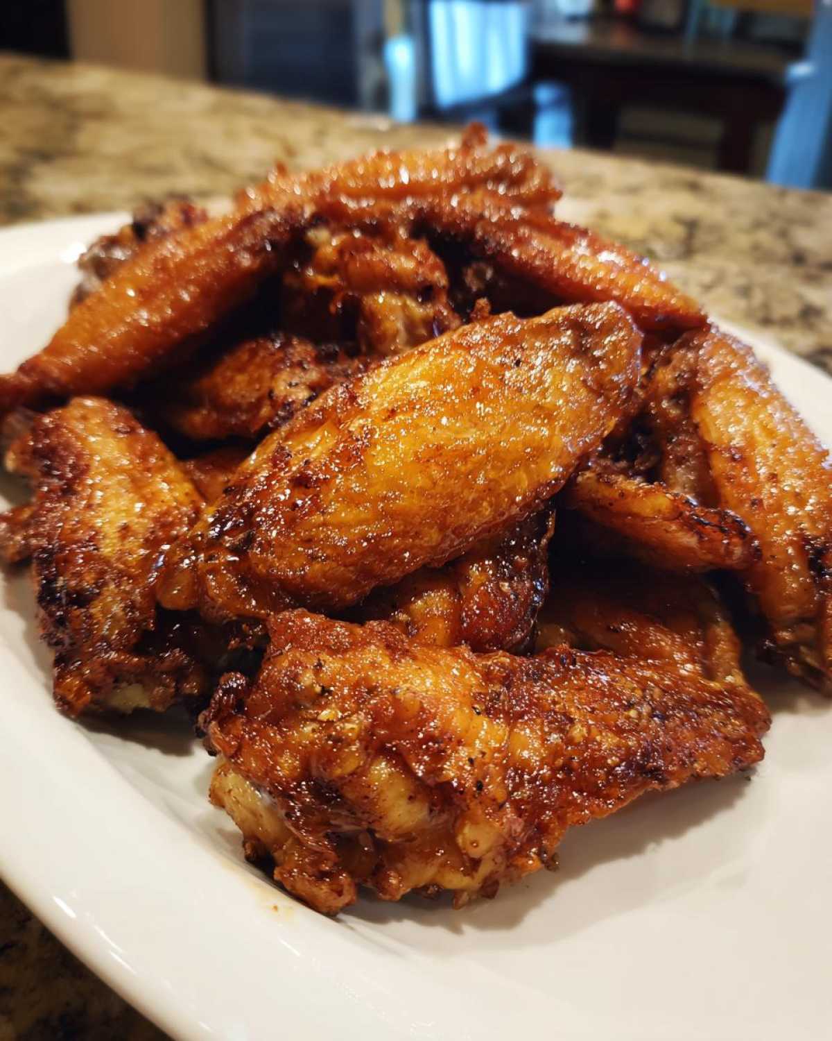 A close-up of perfectly crispy, glazed chicken wings piled high on a white plate.