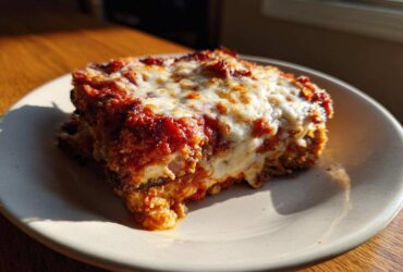 A close-up, sunlit slice of crispy eggplant parmesan layered with rich tomato sauce and melted mozzarella cheese.
