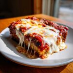 A close-up, appetizing slice of crispy eggplant parmesan covered in rich tomato sauce and gooey, melted mozzarella cheese.