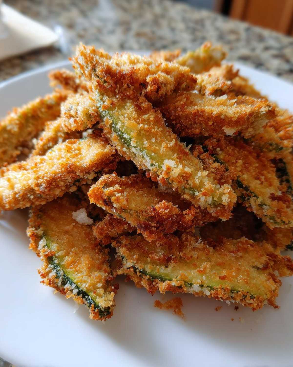 A pile of golden brown, crispy fried pickles slices stacked on a white plate.