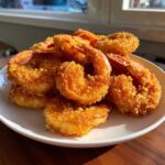A pile of golden brown, crispy fried shrimp with tails on, served on a white plate.