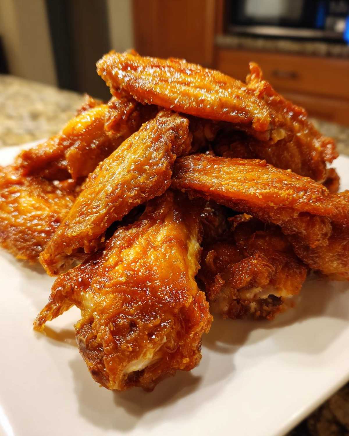 Close-up of a pile of perfectly crispy, glazed chicken wings stacked high on a white plate.