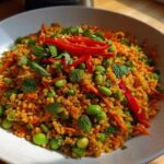 A close-up of a vibrant, seasoned crispy rice salad mixed with bright green edamame, shredded carrots, and fresh mint.