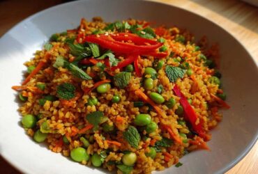 A close-up of a vibrant, seasoned crispy rice salad mixed with bright green edamame, shredded carrots, and fresh mint.