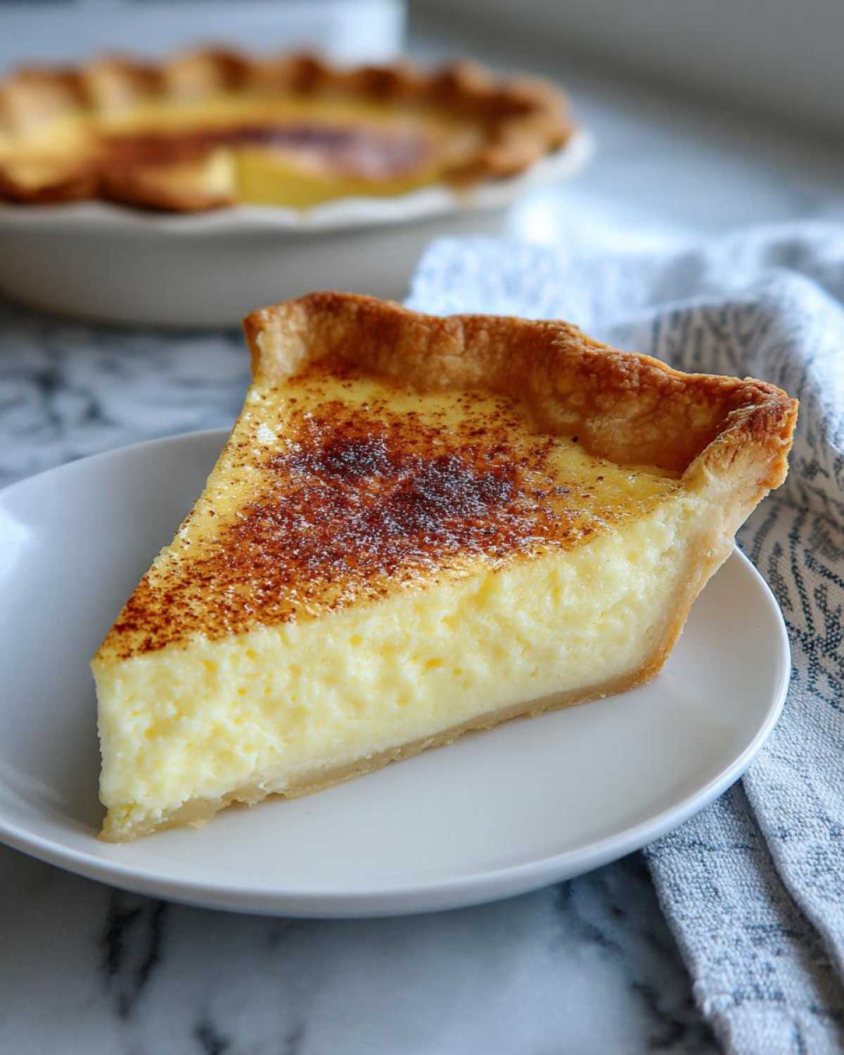A perfect slice of creamy custard pie on a white plate, dusted with nutmeg.