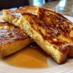 Close-up of thick, golden brown slices of easy french toast drizzled generously with maple syrup on a white plate.