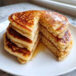 A stack of four fluffy almond flour pancakes, cut to show the interior texture, drizzled with syrup.