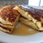 Close-up of a stack of fluffy almond flour pancakes, cut open to show the texture, drizzled with syrup.