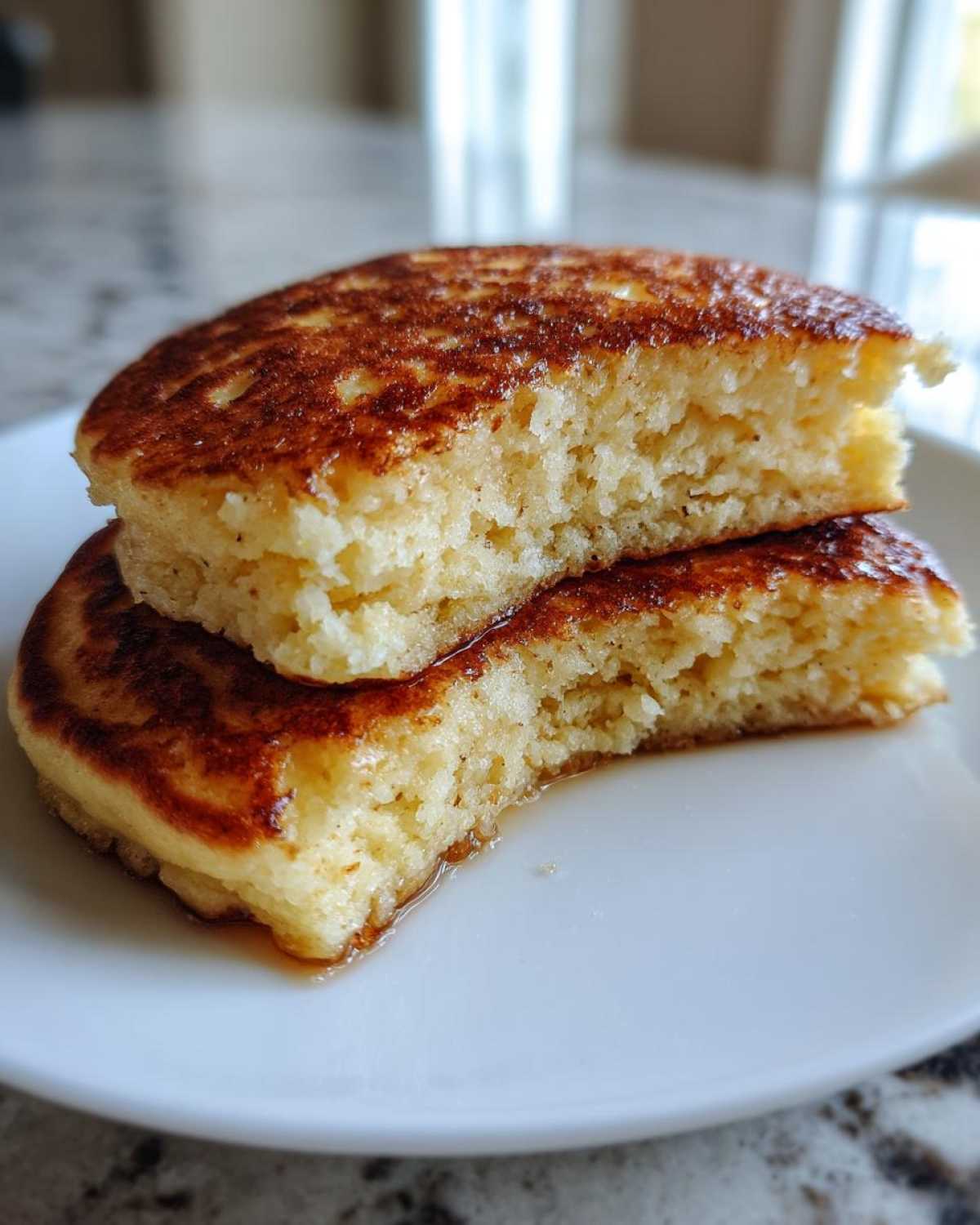 Close-up of two fluffy coconut flour pancakes cut in half, showing the porous interior and golden-brown edges.