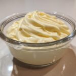 A close-up of freshly made, creamy homemade mayonnaise swirled beautifully in a clear glass serving bowl.