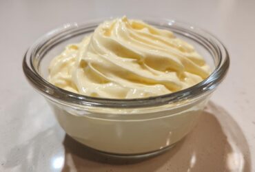 A close-up of freshly made, creamy homemade mayonnaise swirled beautifully in a clear glass serving bowl.