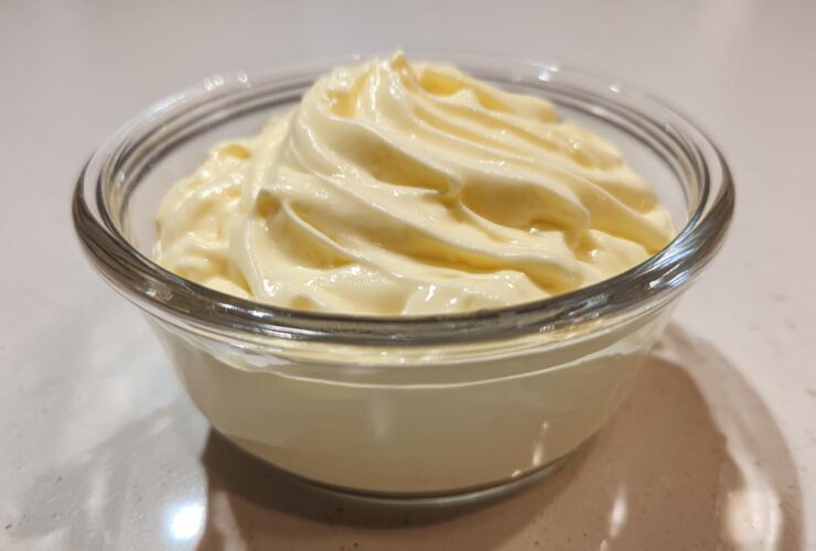A close-up of freshly made, creamy homemade mayonnaise swirled beautifully in a clear glass serving bowl.