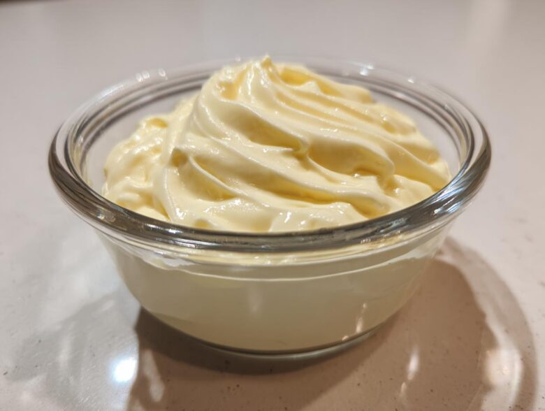 A close-up of freshly made, creamy homemade mayonnaise swirled beautifully in a clear glass serving bowl.