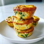 A stack of three fluffy muffin tin egg bites with visible green spinach pieces, served on a white plate.
