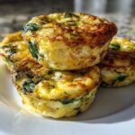 A stack of four fluffy muffin tin egg bites, featuring visible spinach and golden-brown tops, served on a white plate.