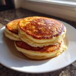 A stack of three perfectly golden brown, fluffy pancakes sitting on a white plate.