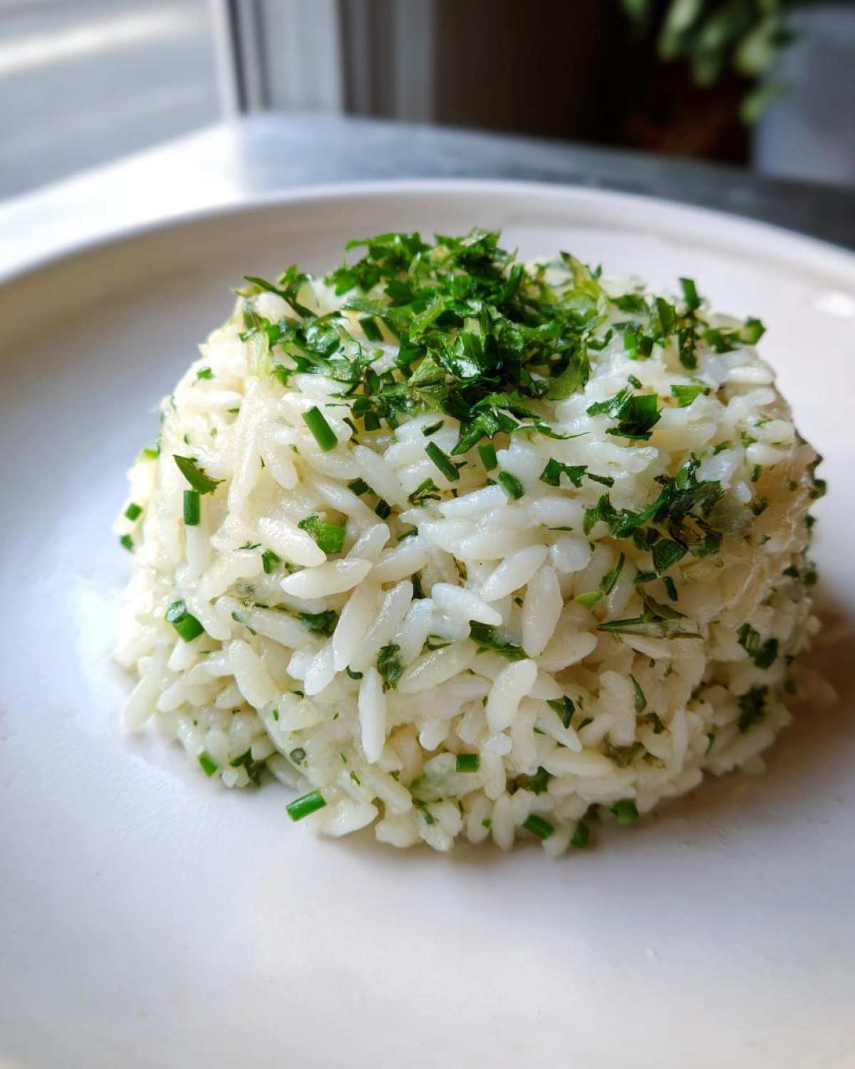 A mound of fluffy white rice pilaf seasoned with green herbs, served on a white plate.