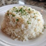 A mound of fluffy, white rice pilaf garnished with chopped fresh parsley served on a white plate.